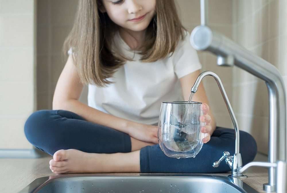 girl filling water glass at kitchen sink